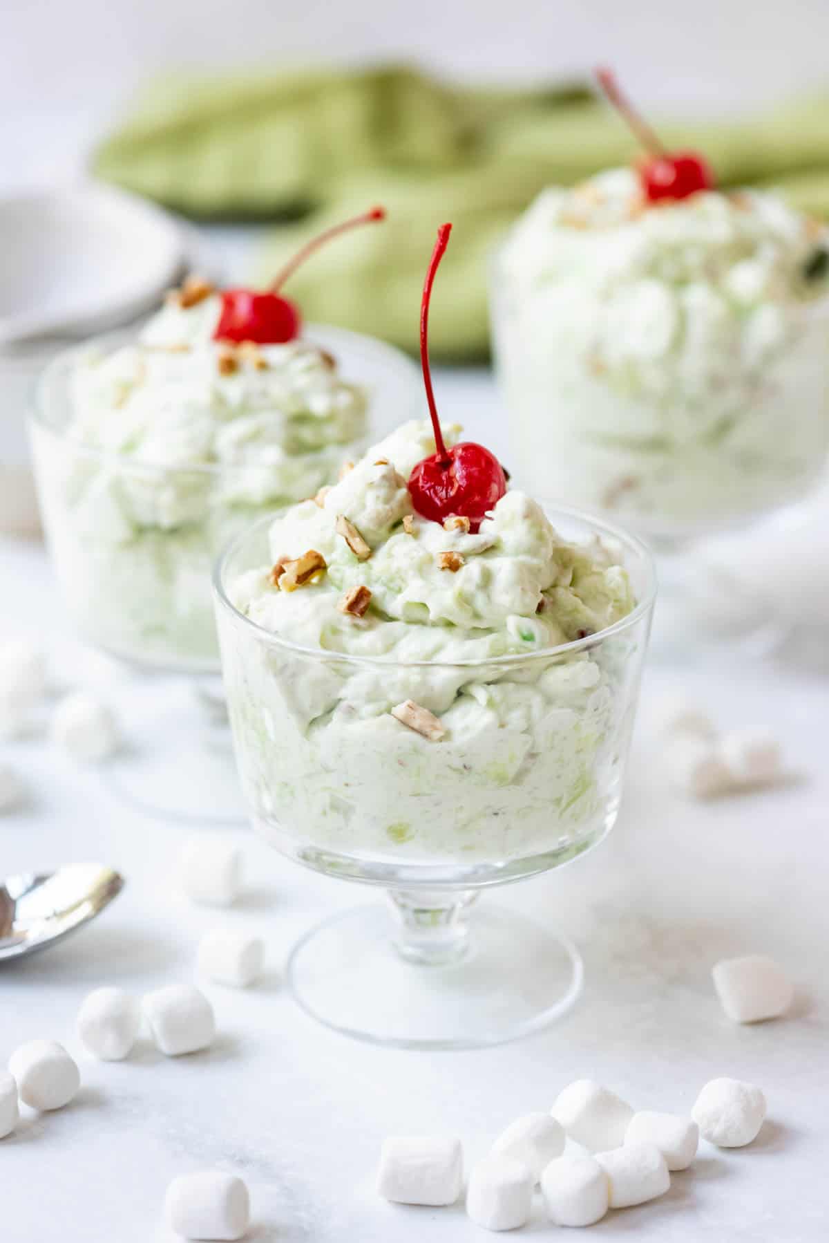Three glass bowls of watergate salad decorated with a maraschino cherry on top.