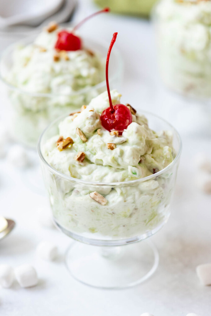 Two glass dessert bowls filled with watergate salad with maraschino cherries on top.