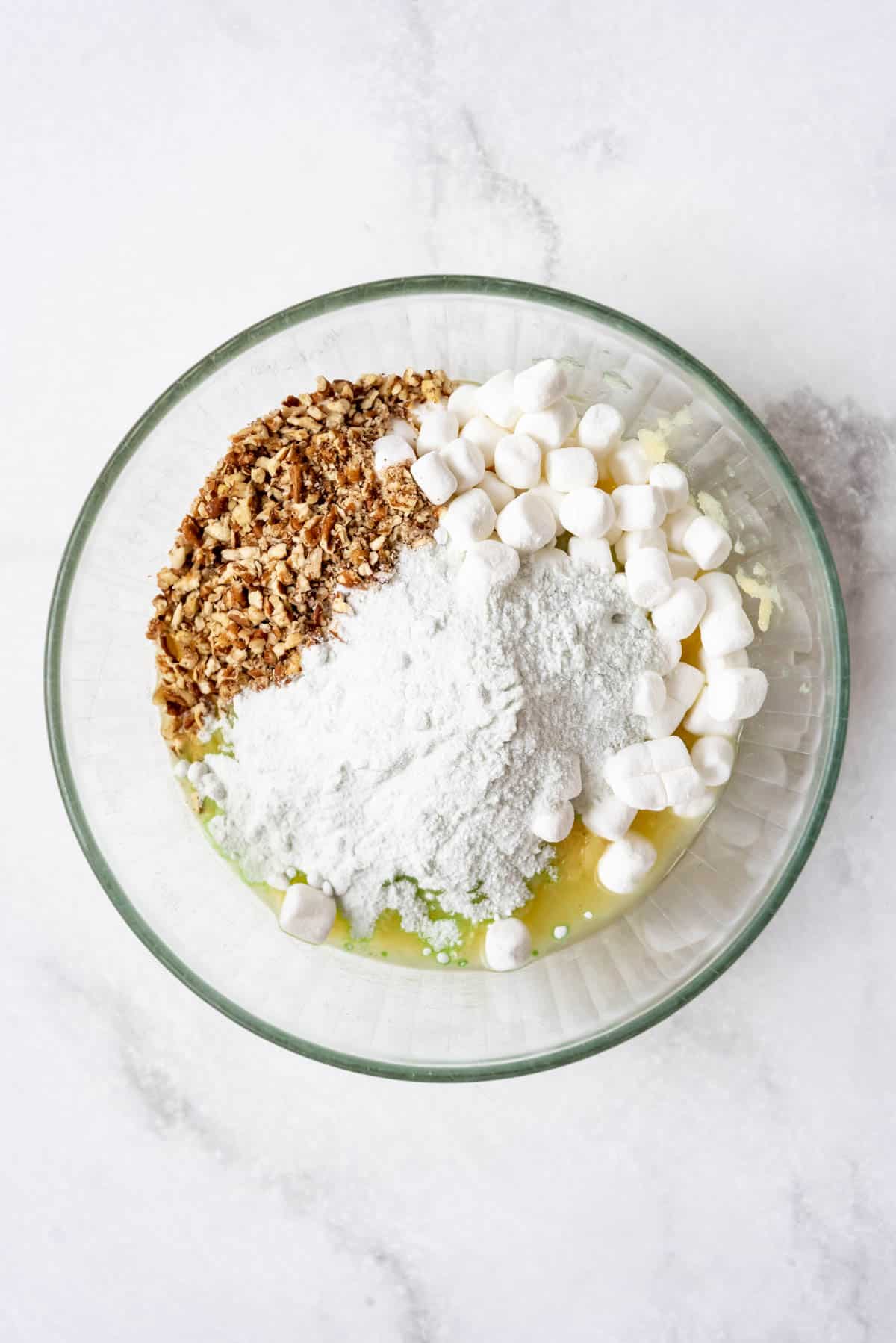 Crushed pineapple, chopped pecans, marshmallows, and instant pistachio pudding mix in a glass bowl.
