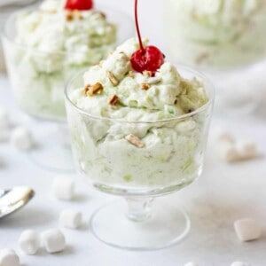 Glass dessert bowls filled with creamy pistachio and marshmallow watergate salad with a maraschino cherry on top.