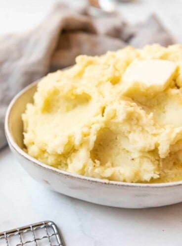 Close up of mashed potatoes in a serving dish with a small block of butter on top.