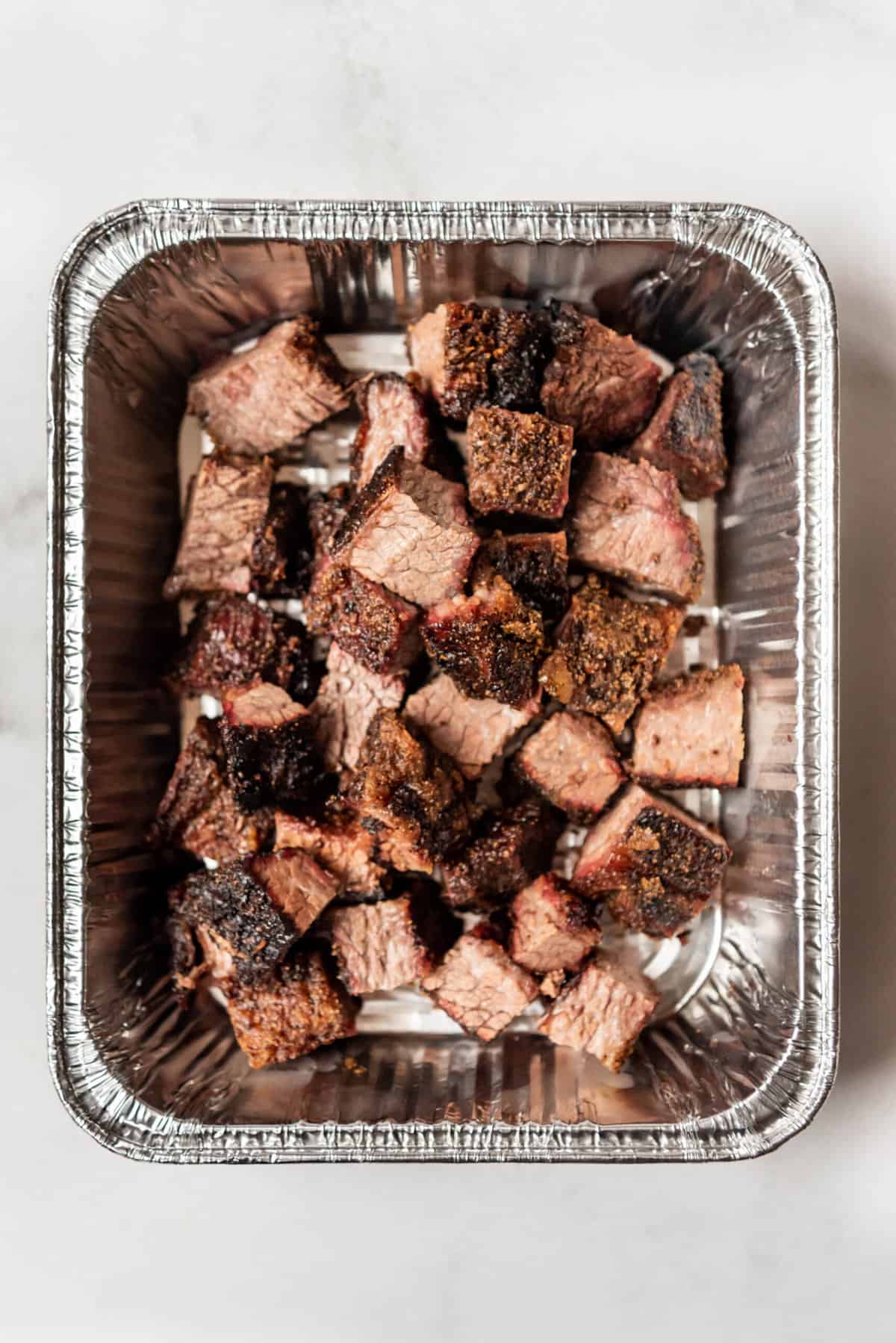 A disposable aluminum pan filled with chunks of sliced beef brisket for burnt ends.