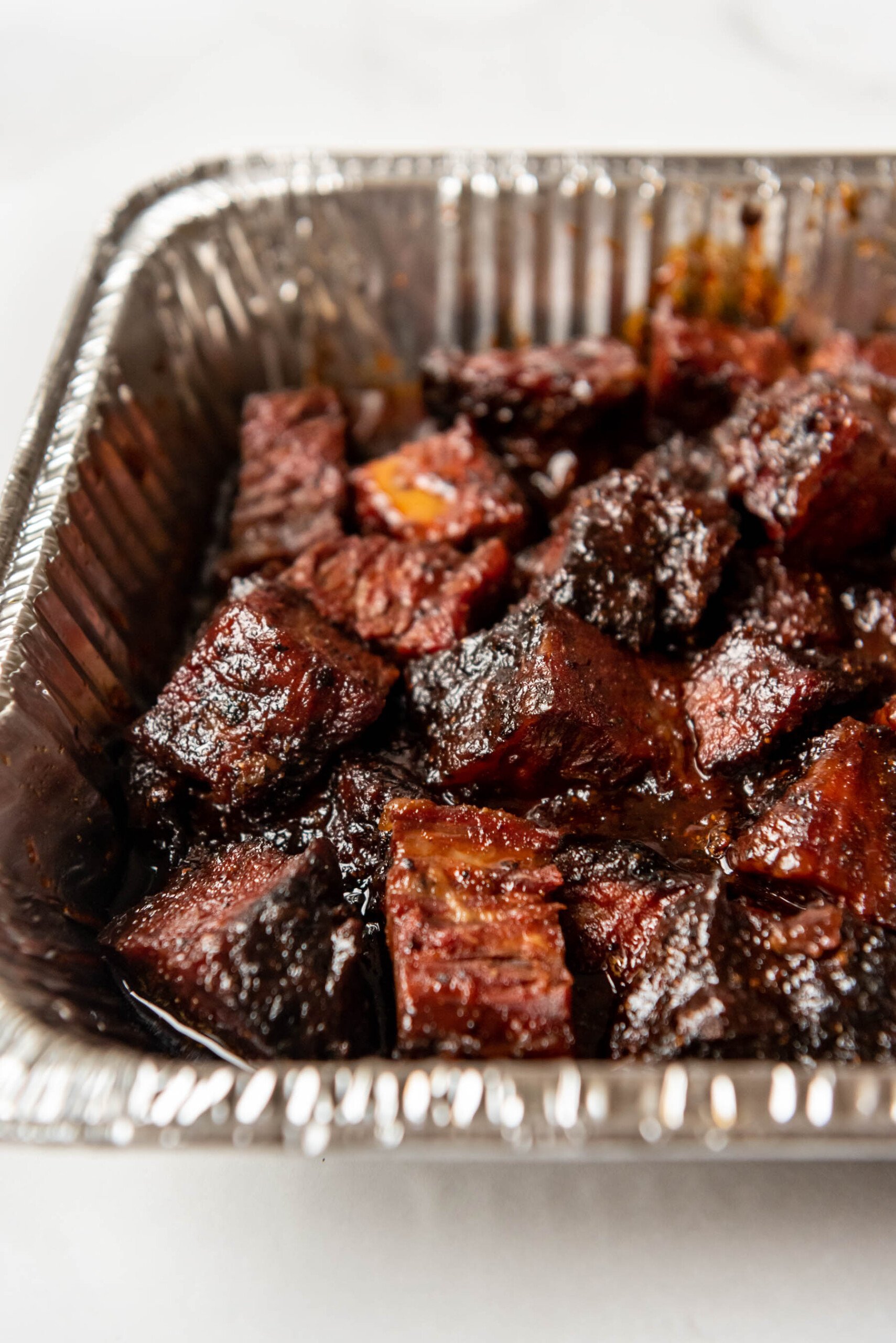A close image of sticky BBQ brisket burnt ends in an aluminum pan.