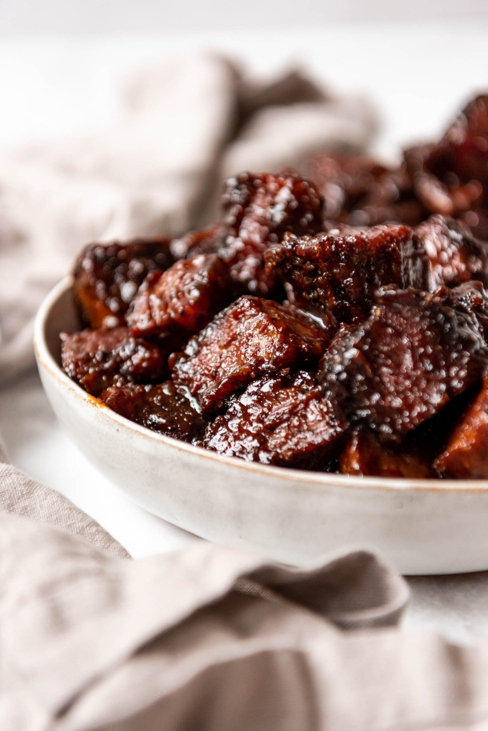 Beef brisket burnt ends piled in a bowl next to a cloth napkin.