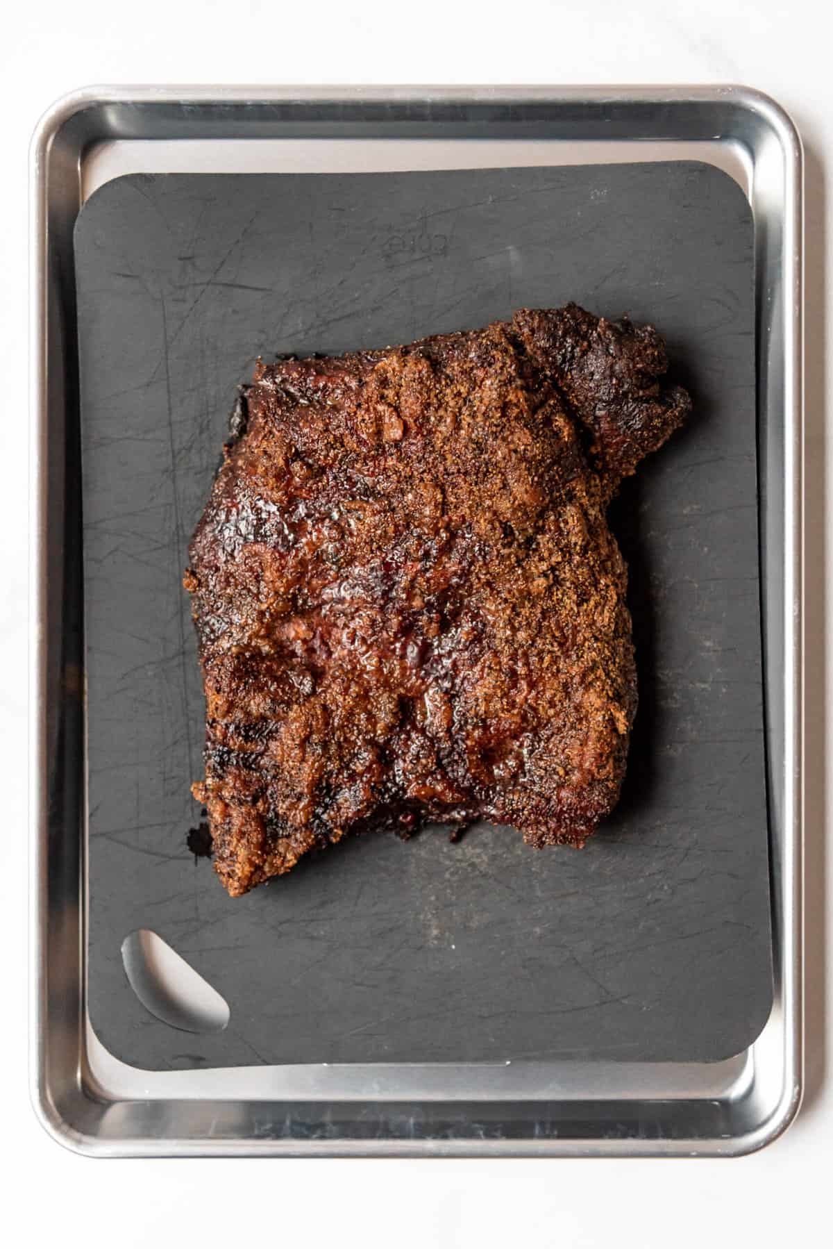 A cooked beef brisket point on a grey baking sheet.