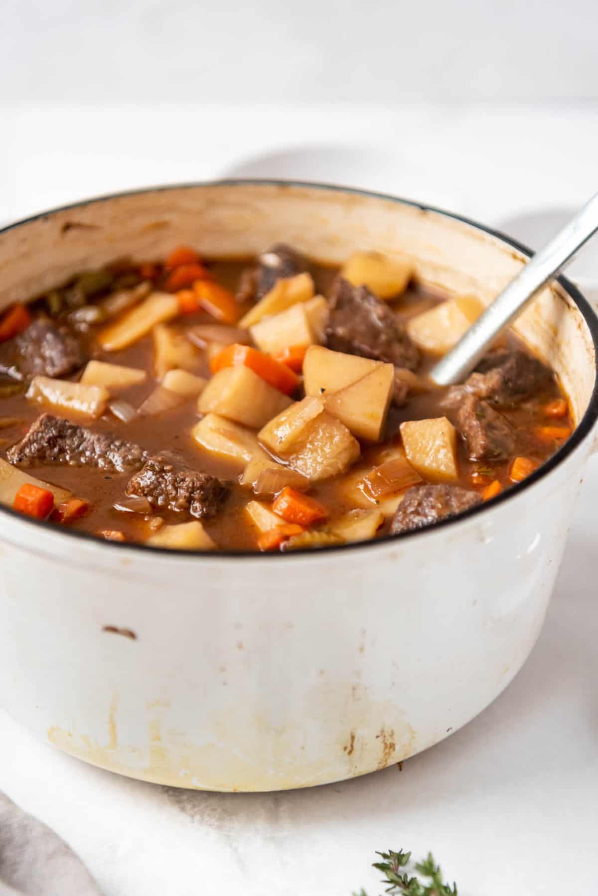 A close image of hearty beef stew in a white dutch oven pot.