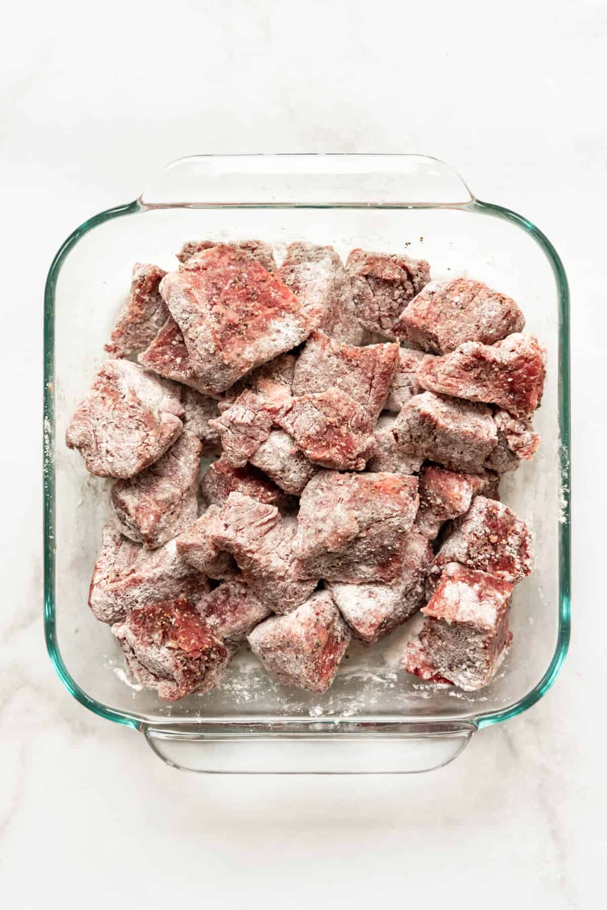 Beef stew meat dredged in flour, salt, and pepper in a glass dish.