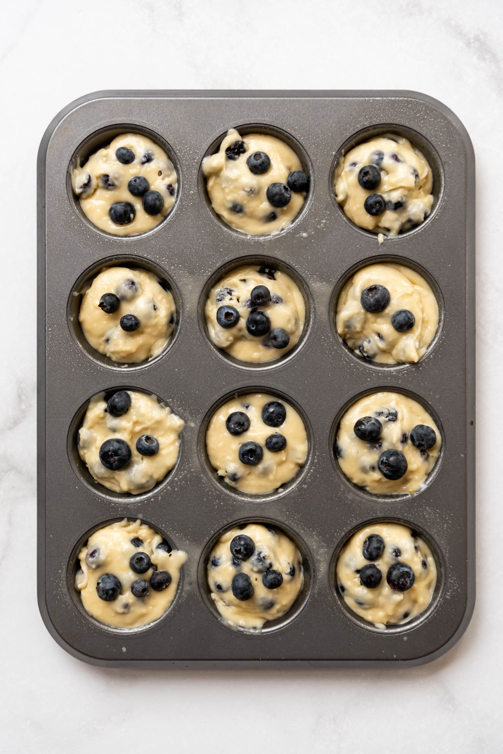 A 12-count muffin pan filled with blueberry muffin batter.