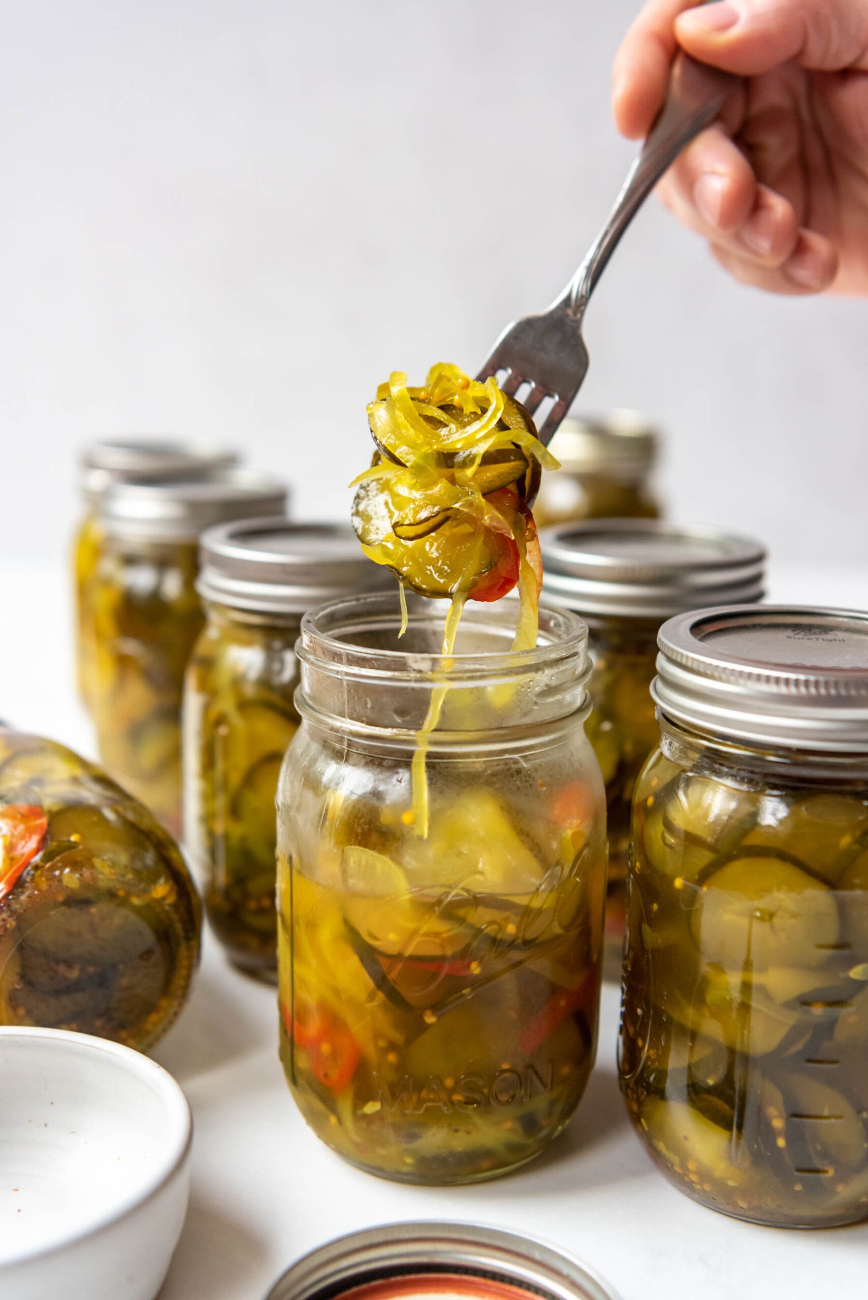 A hand lifting a forkful of bread and butter pickles out of a jar.