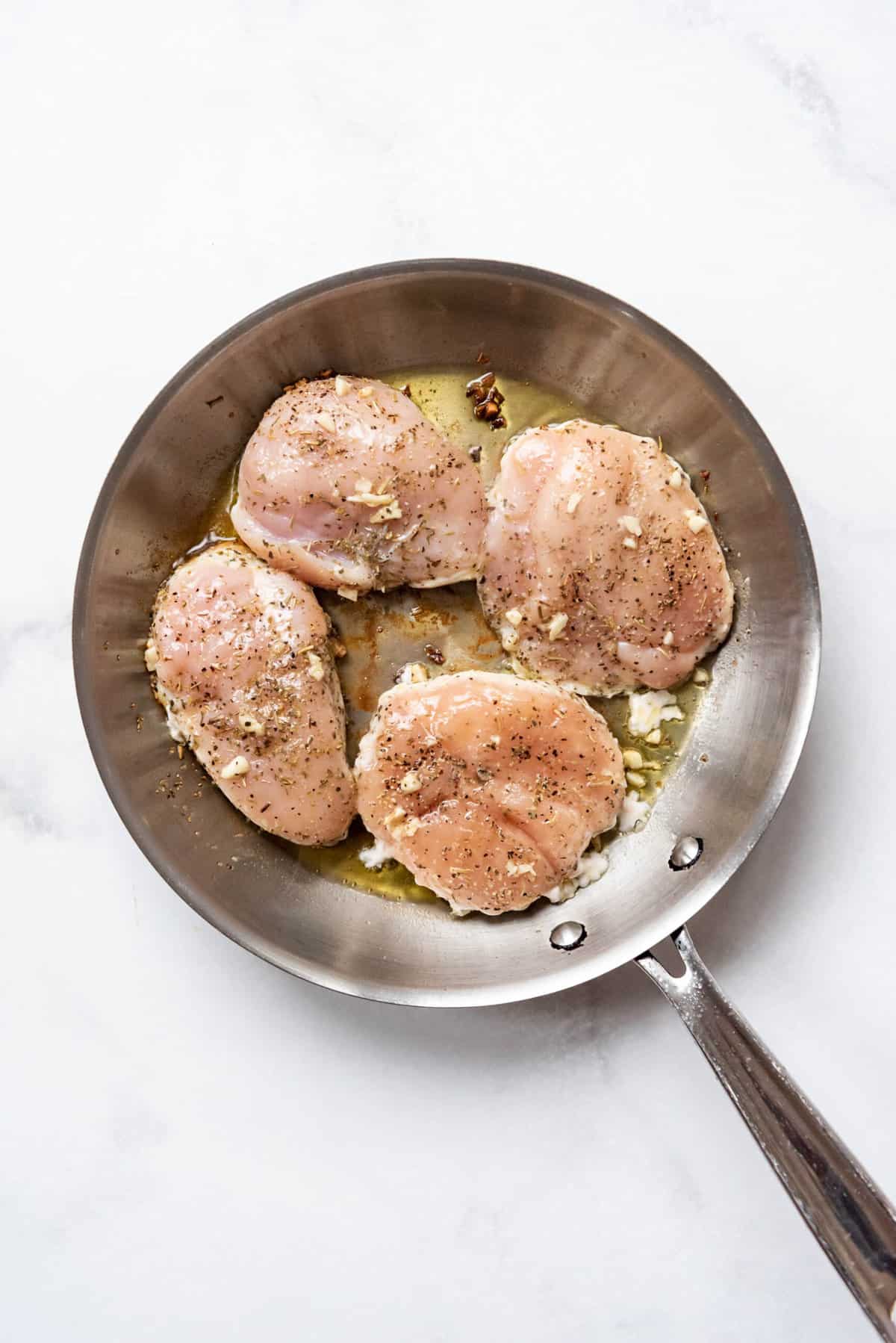 Four boneless skinless chicken breasts in a pan with hot oil.