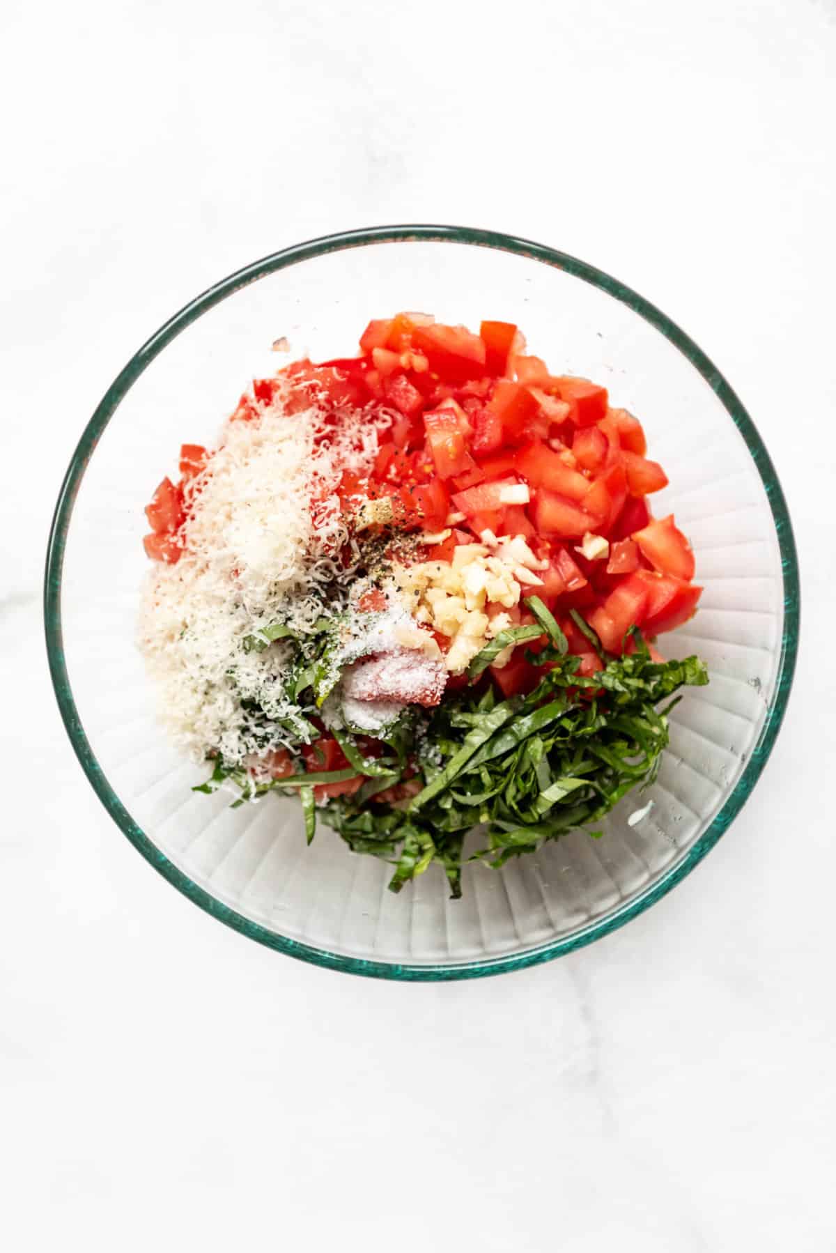 Chopped tomatoes, strips of fresh basil, garlic, and Parmesan cheese in a bowl.