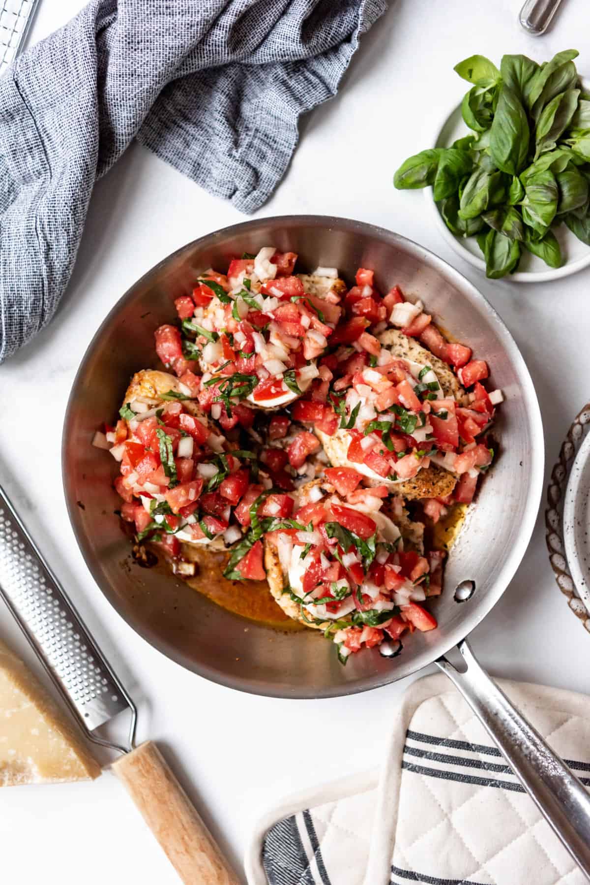 Chicken breasts topped with bruschetta topping in a pan.