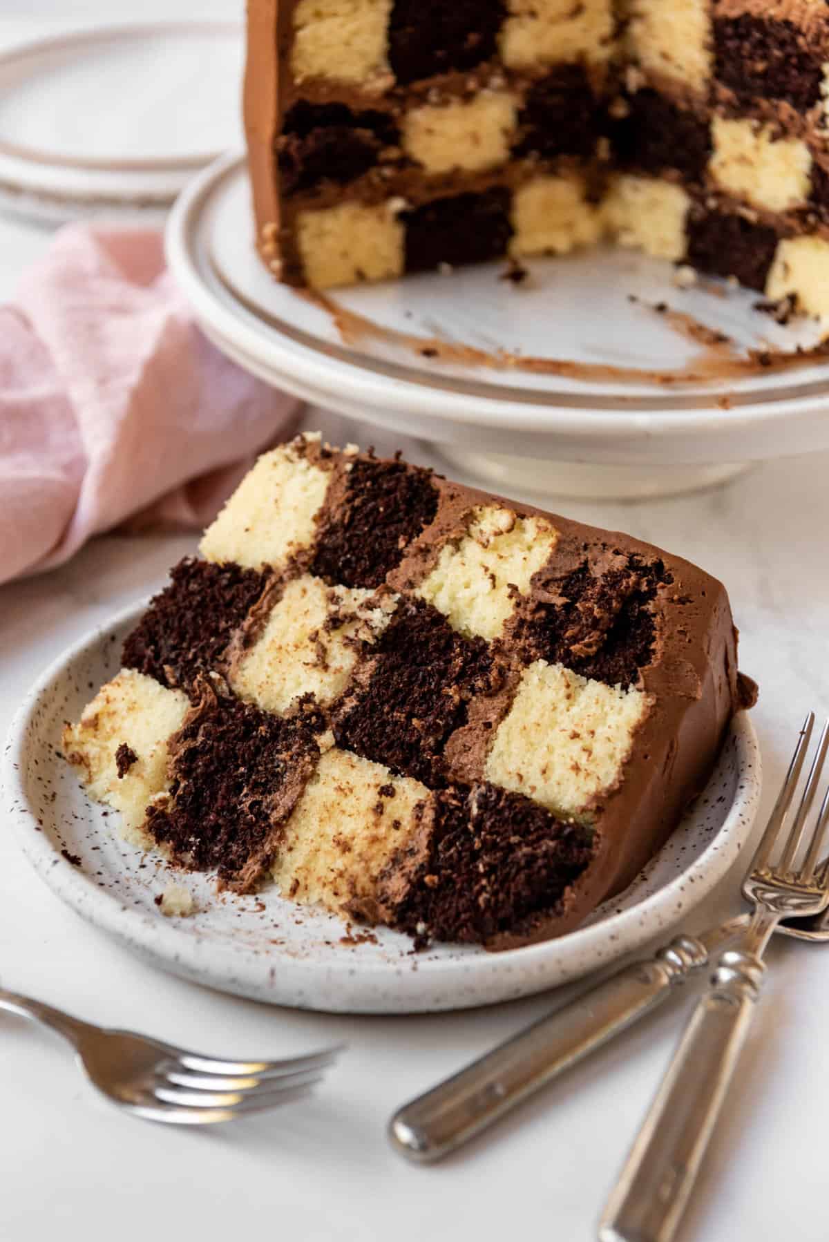 A slice of checkerboard cake on a white plate next to forks.