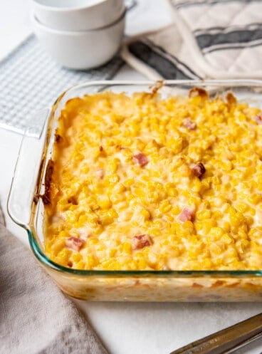 A glass baking dish of cheesy corn with ham.