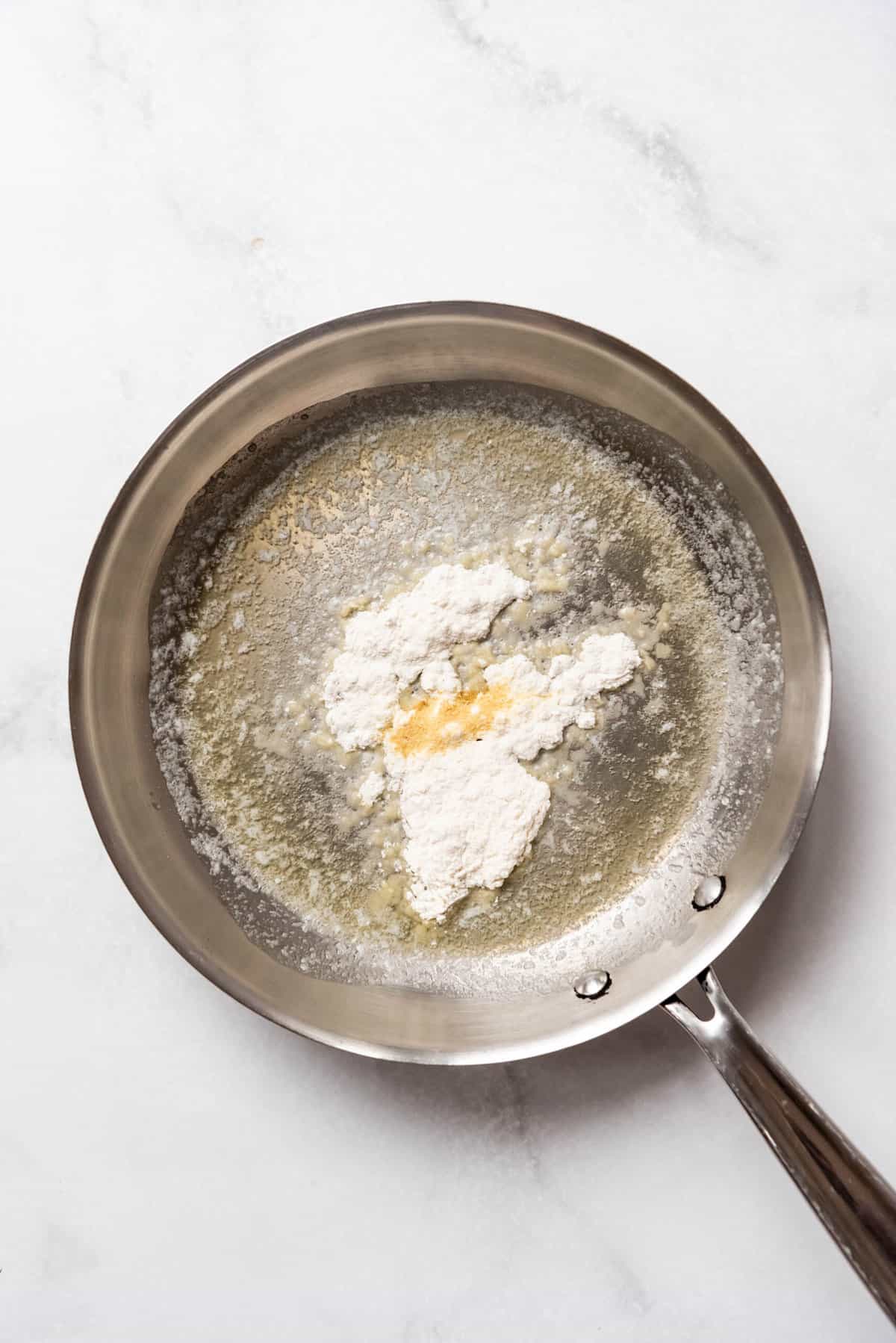 Adding flour to melted butter in a pan to make a roux.