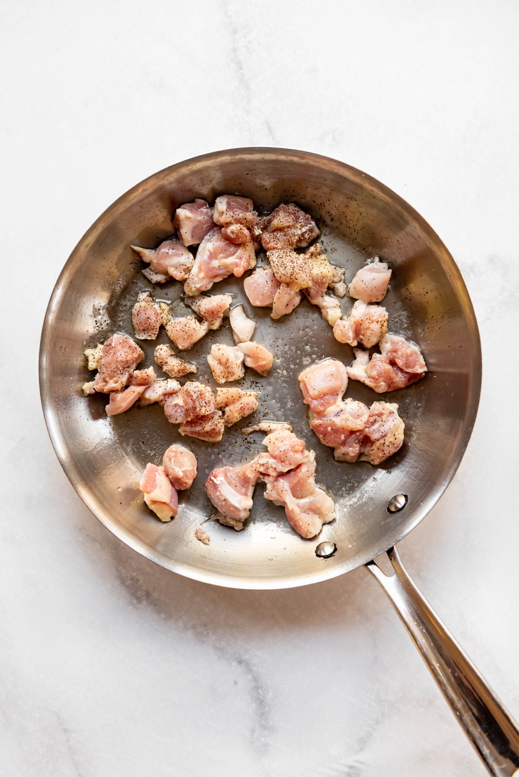 Searing small pieces of chicken in oil in a pan.