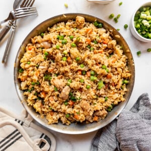 A large pan of chicken fried rice surrounded by forks, a cloth napkin, and hot pads.