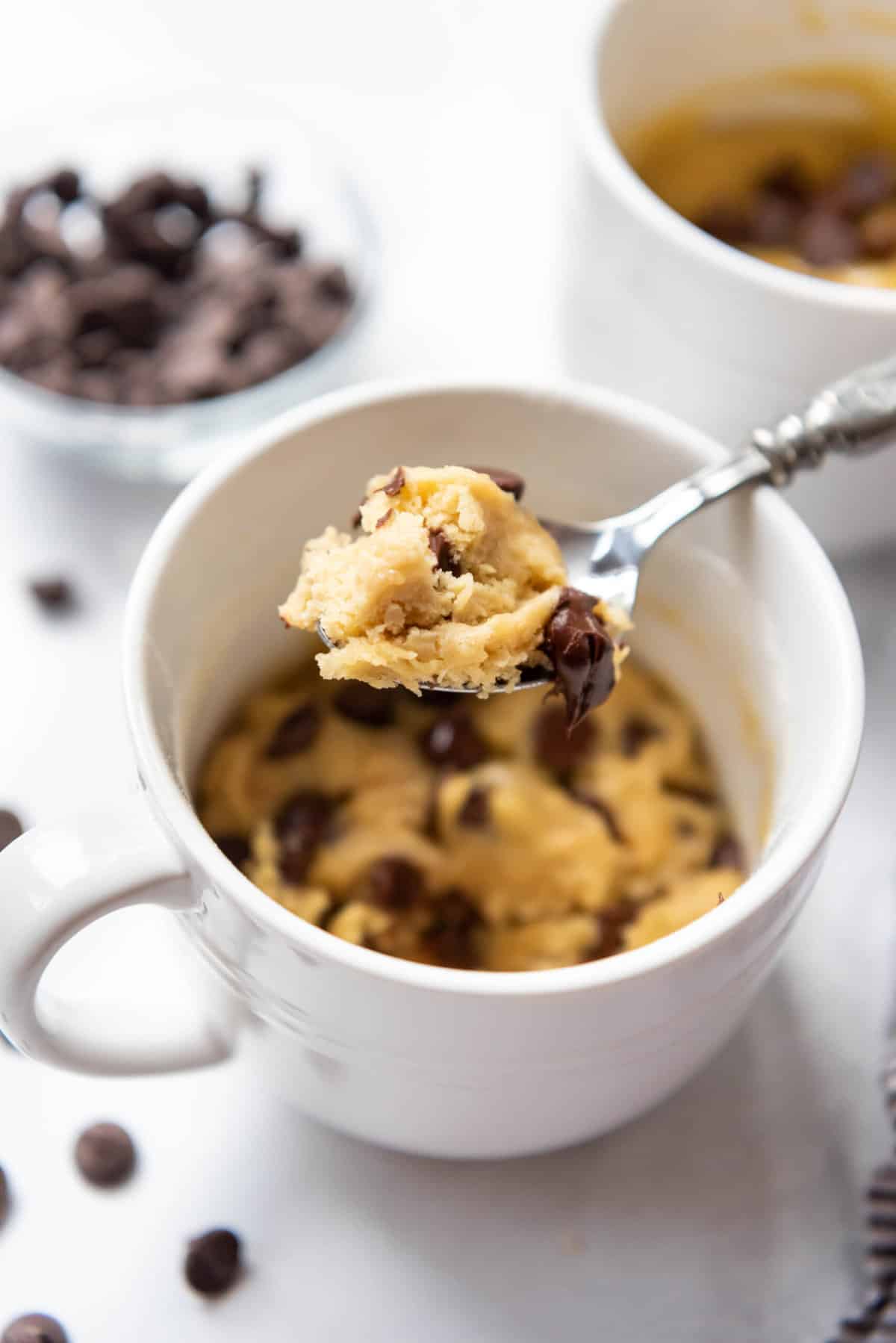 A spoon lifting a bite of chocolate chip cookie made in a mug.