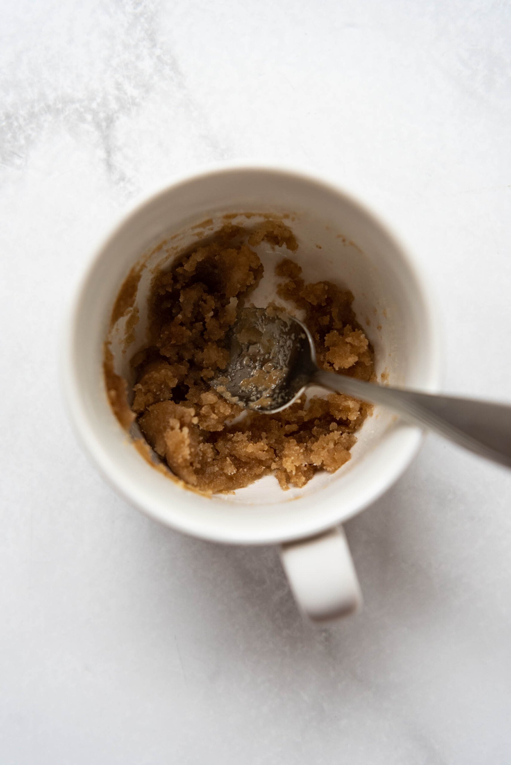 Stirring butter and sugars together with a spoon in a white mug.