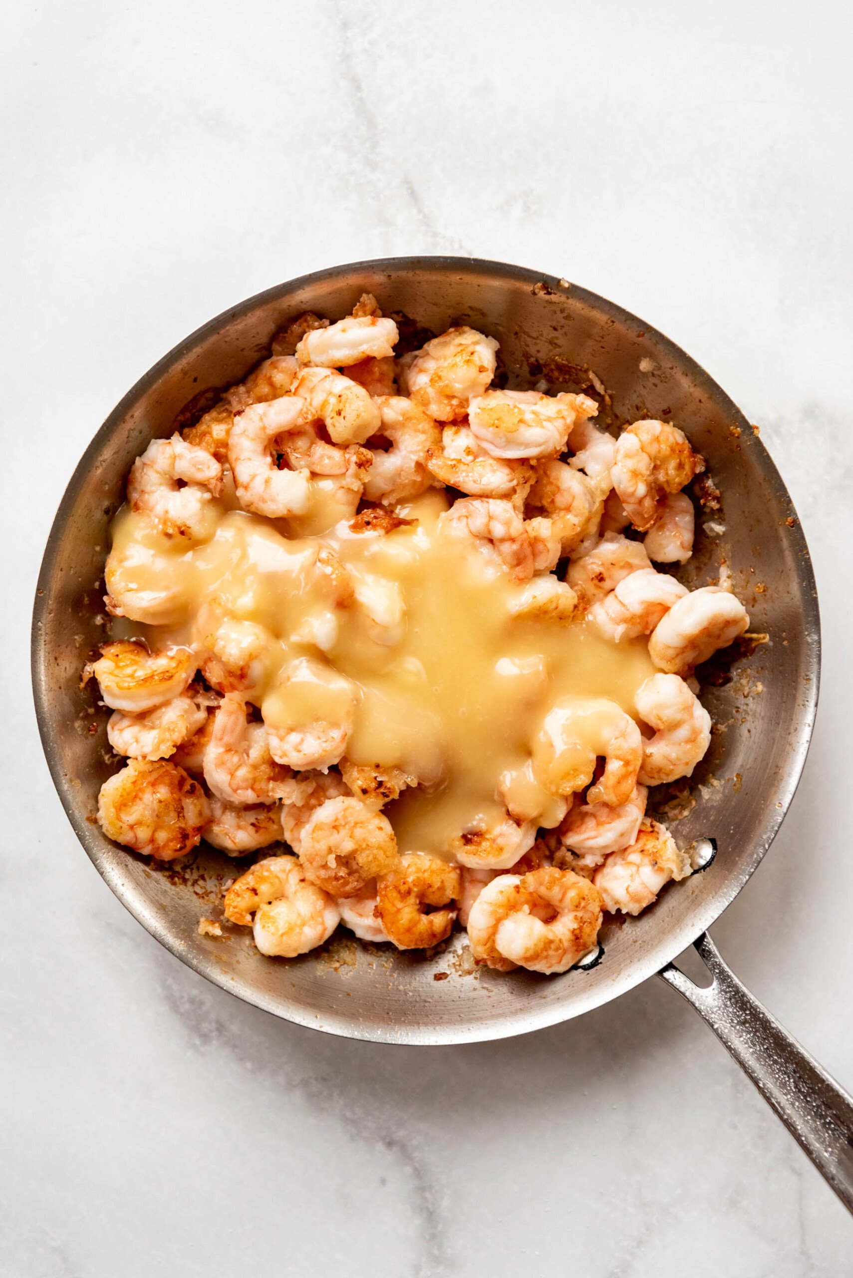 Adding honey mayo sauce to cooked crispy shrimp to make honey walnut shrimp.
