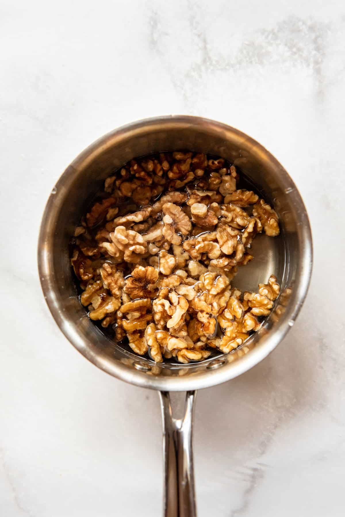 Whole walnuts in a saucepan with sugar and water.