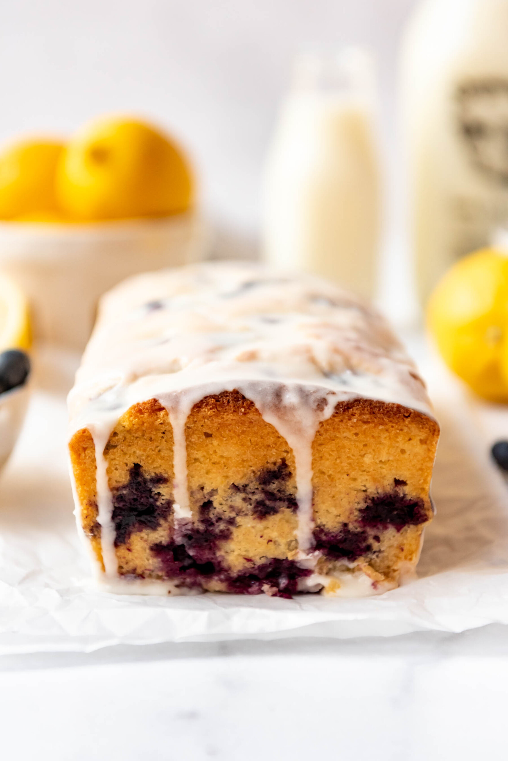 A glazed loaf of homemade lemon blueberry bread on white parchment paper.