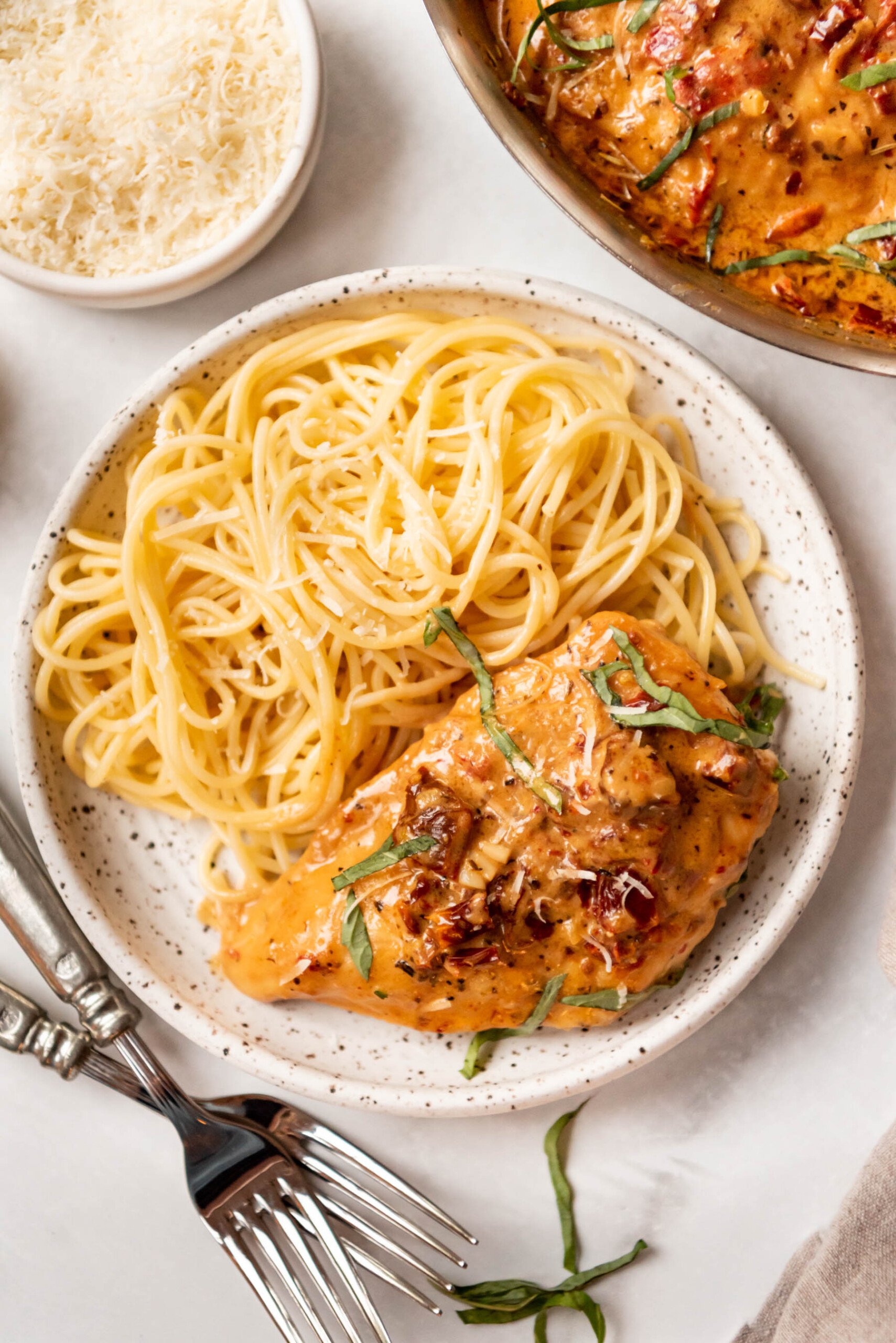 A plate of cooked spaghetti with a chicken breast in creamy sundried tomato sauce.
