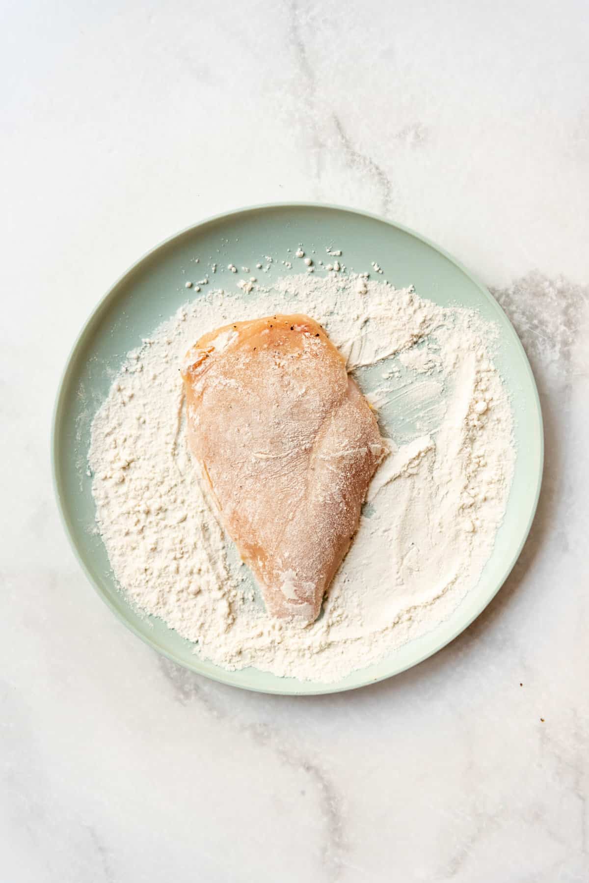 Dredging a chicken breast cutlet in flour.