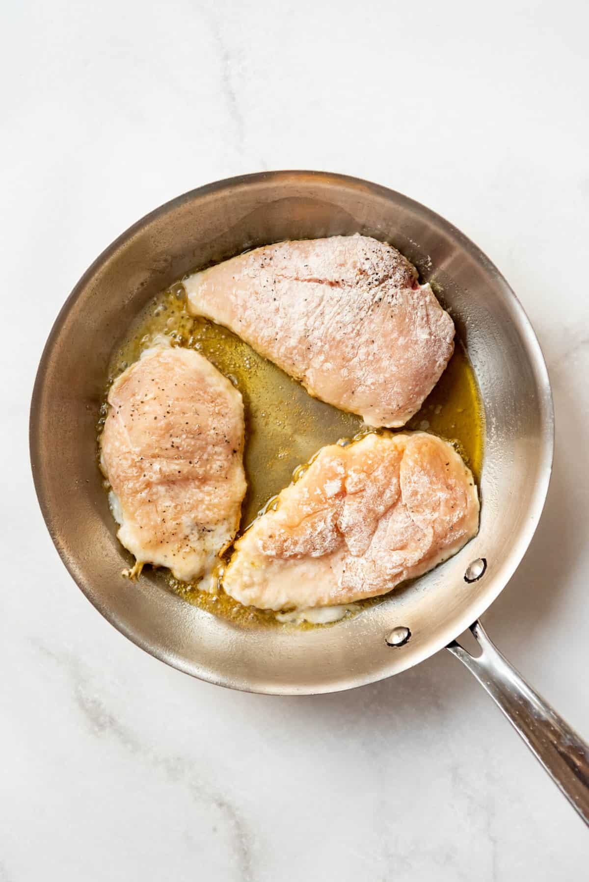 Searing chicken breasts in oil in a pan.