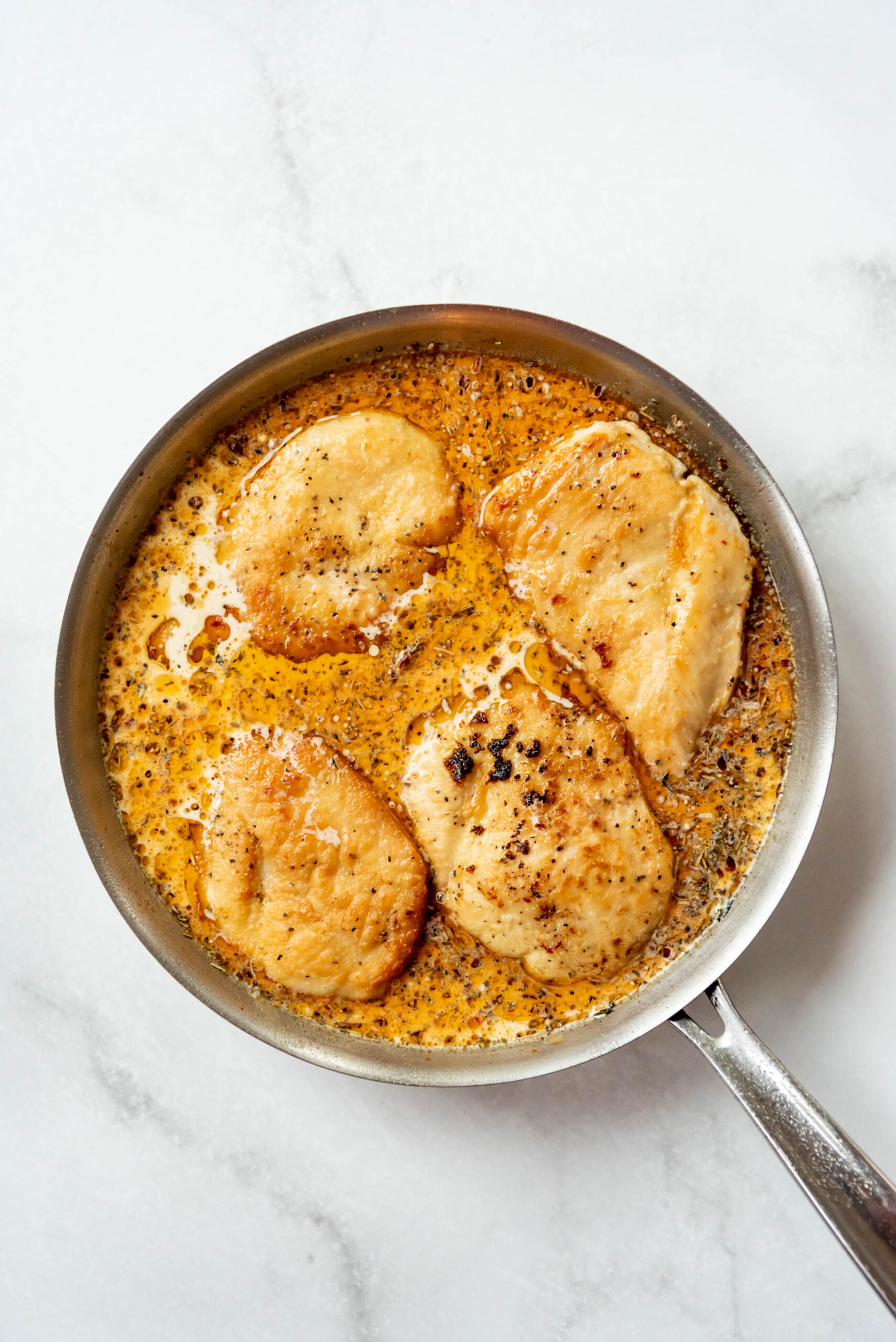 Returning seared chicken breasts to a pan with a creamy sundried tomato sauce.