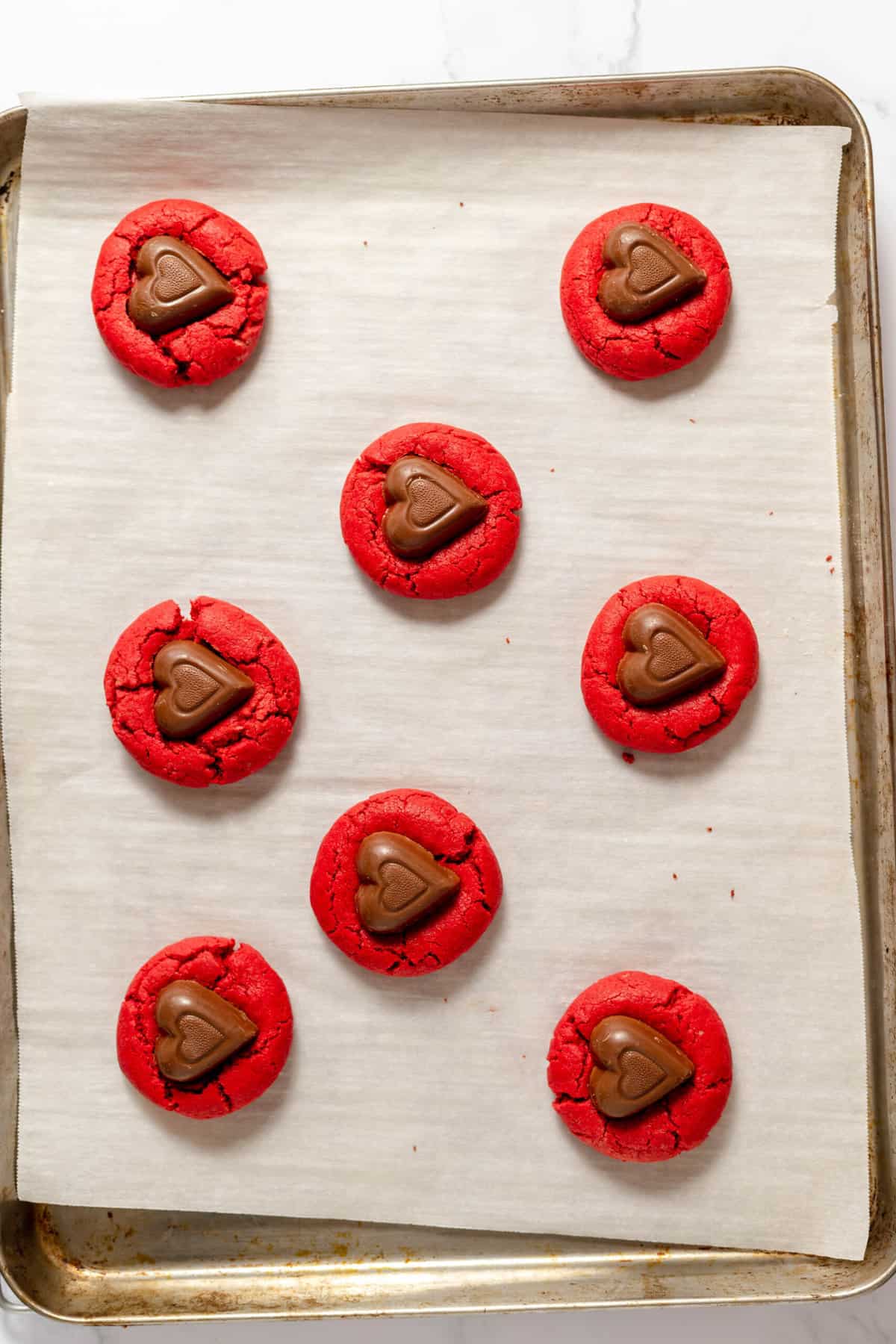 Adding unwrapped dove chocolate hearts on top of soft red velvet cookies on a baking sheet lined with parchment paper.