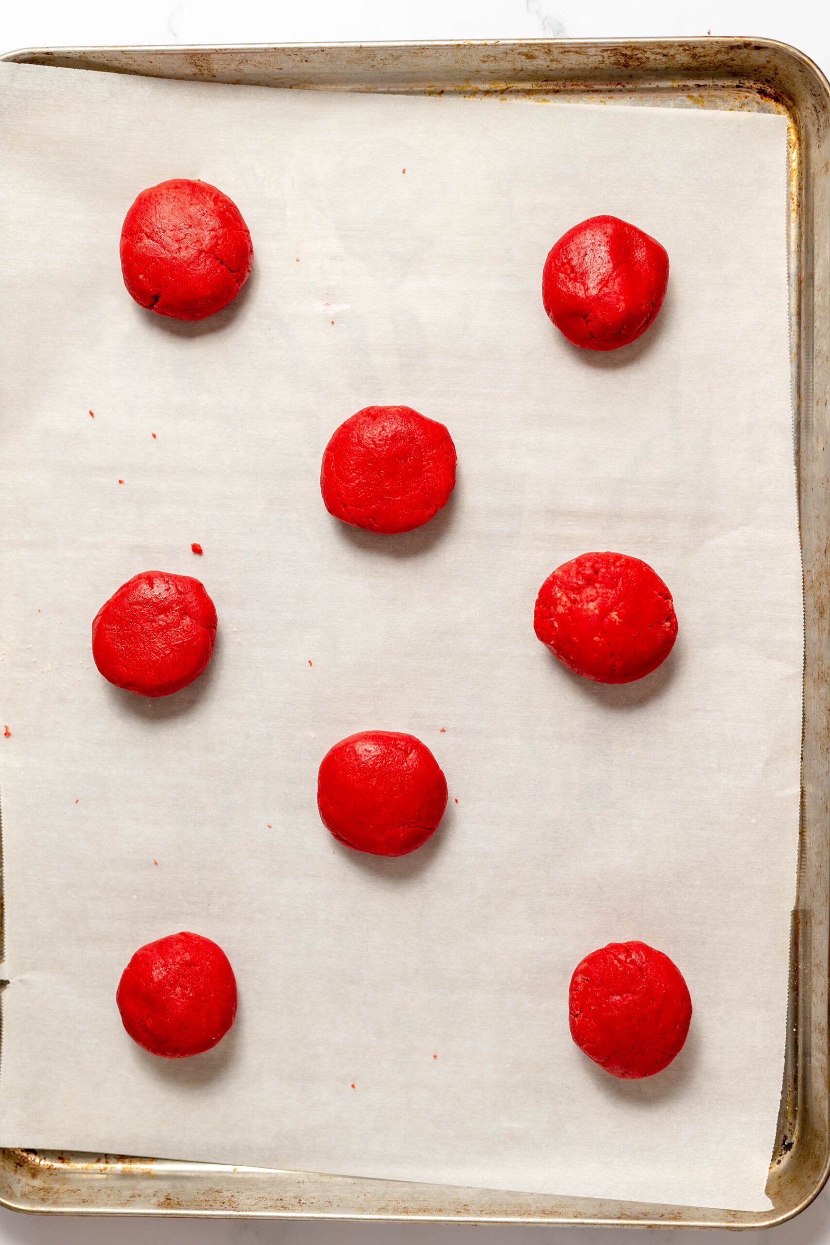 Red velvet cookie dough balls on a baking sheet lined with parchment paper.