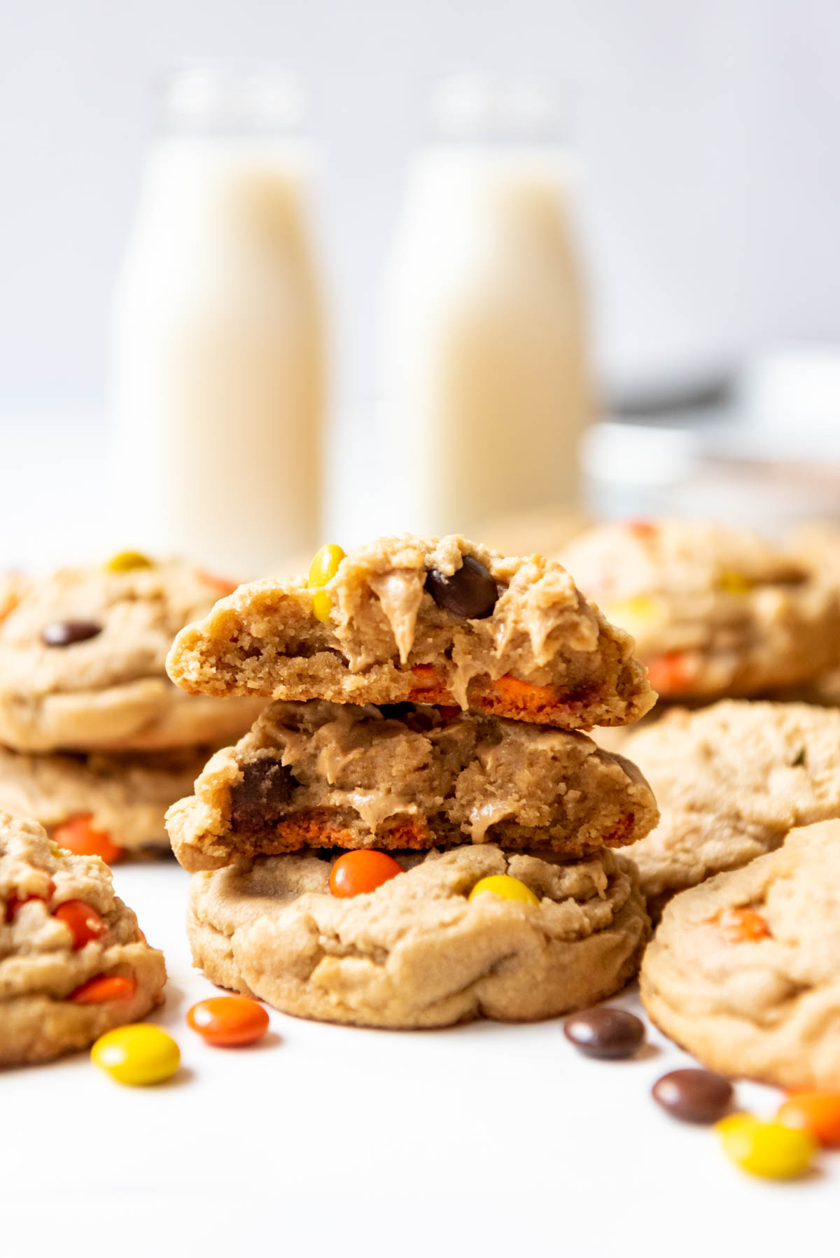 A Reese's Pieces cookie that has been broken in half and stacked on top of another cookie with two glasses of milk in the background.