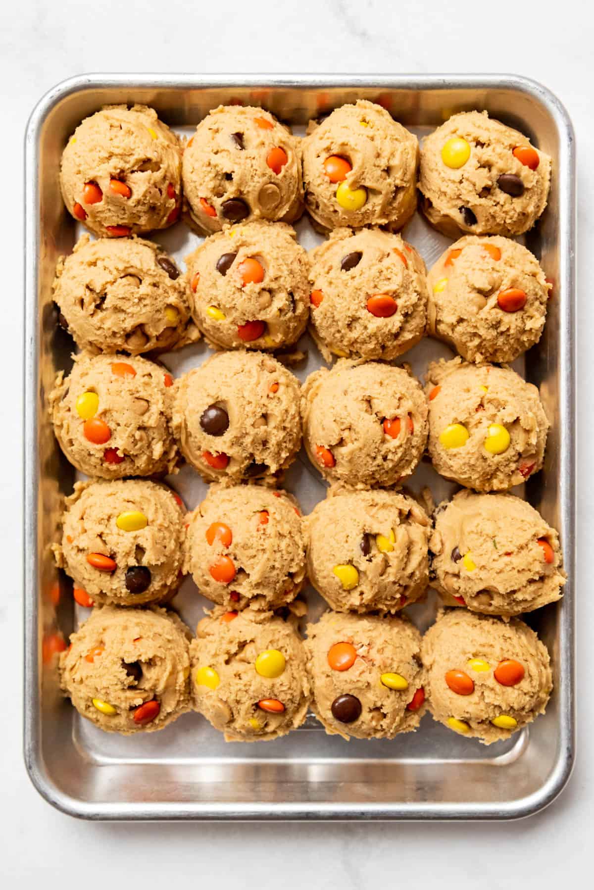An overhead image of balls of peanut butter cookie dough with Reese's Pieces on a baking sheet.