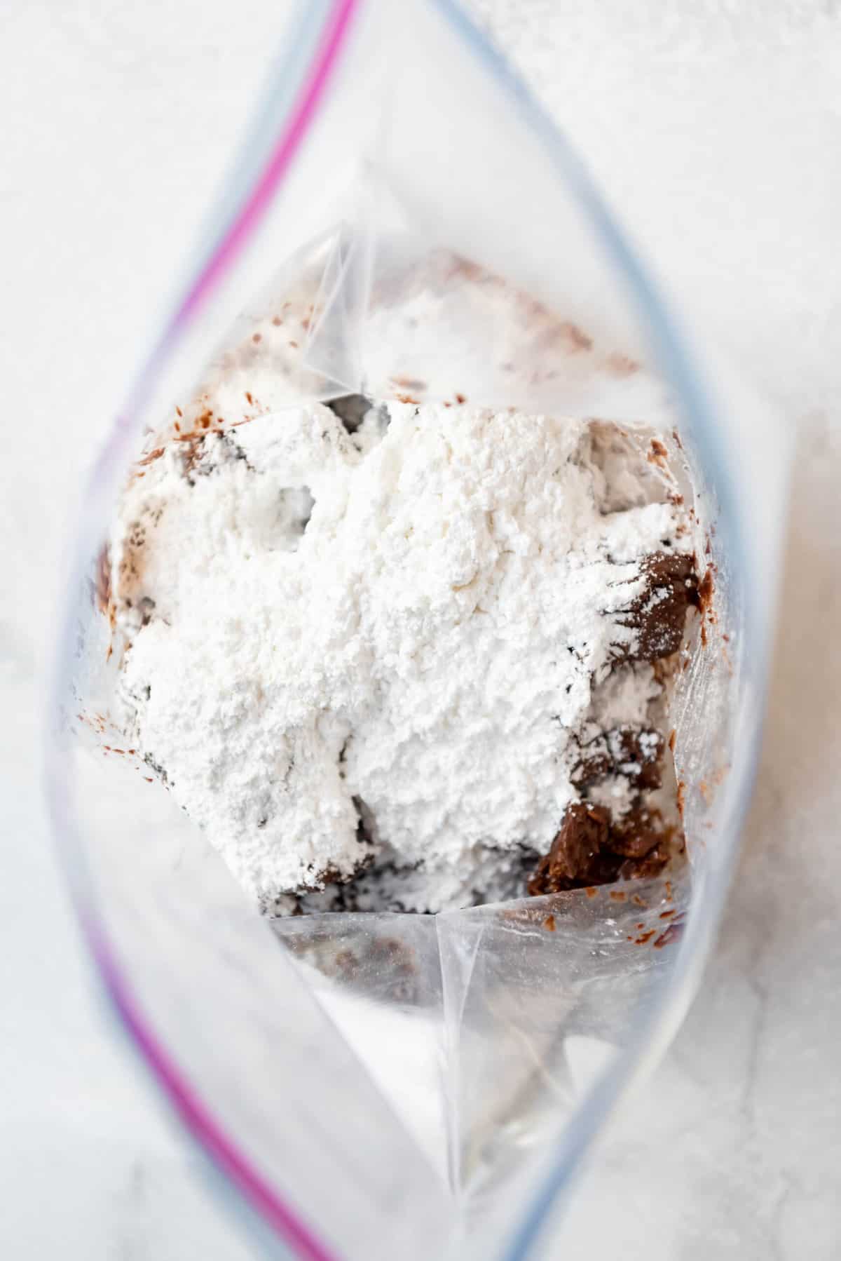 An image of powder sugar in a bag with chocolate and cereal for muddy buddies.