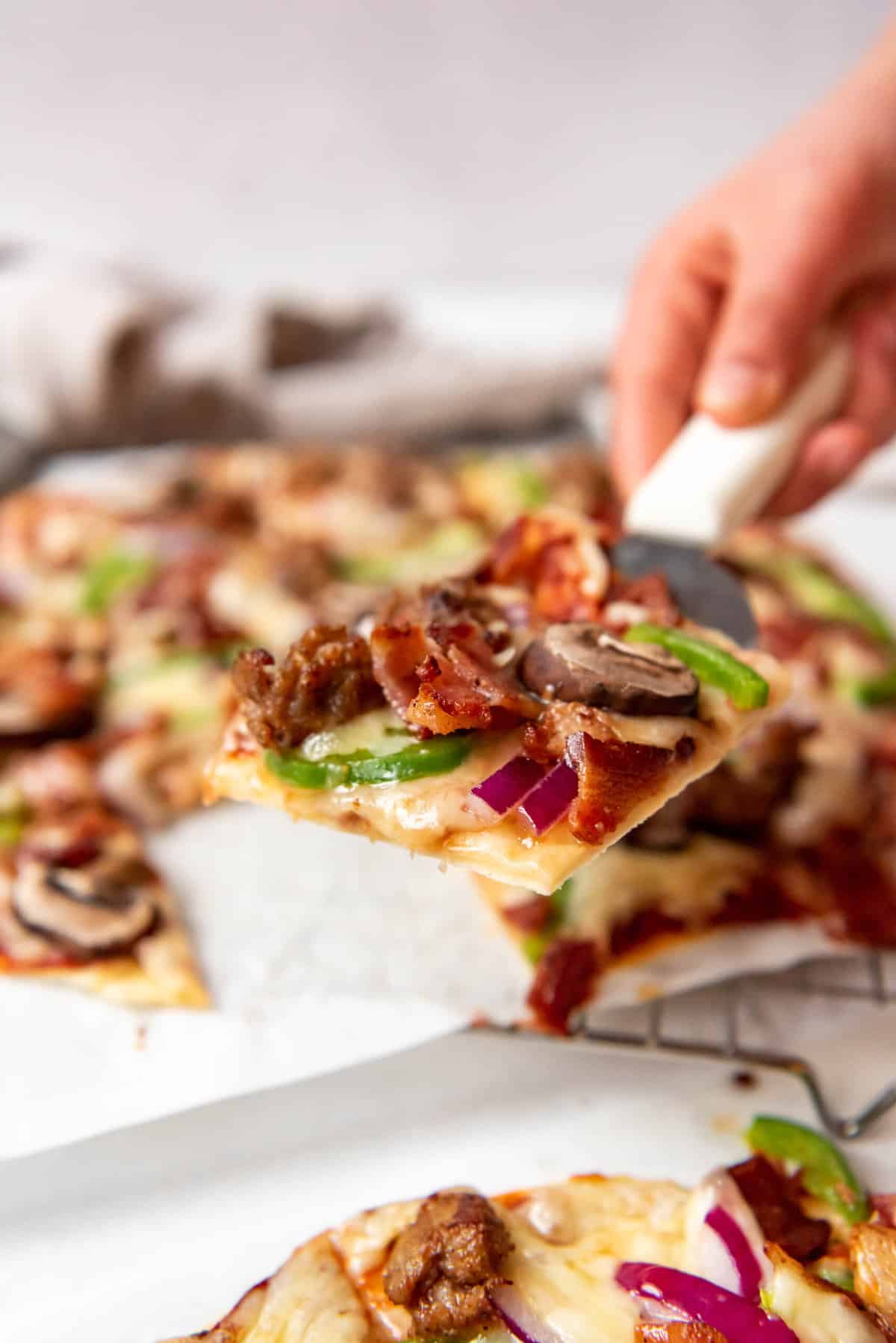 A hand lifting a slice of St. Louis-style pizza on a spatula.