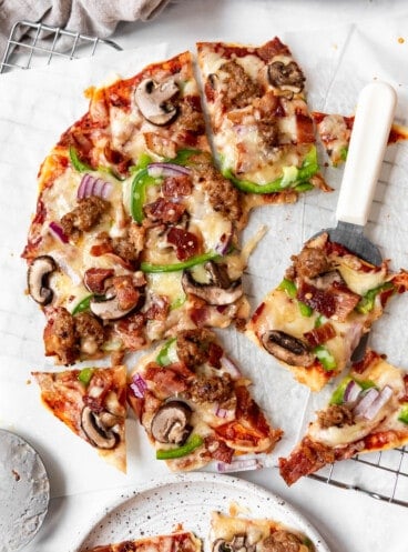 A deluxe St. Louis-style pizza cut into squares with one piece on a white handled spatula.