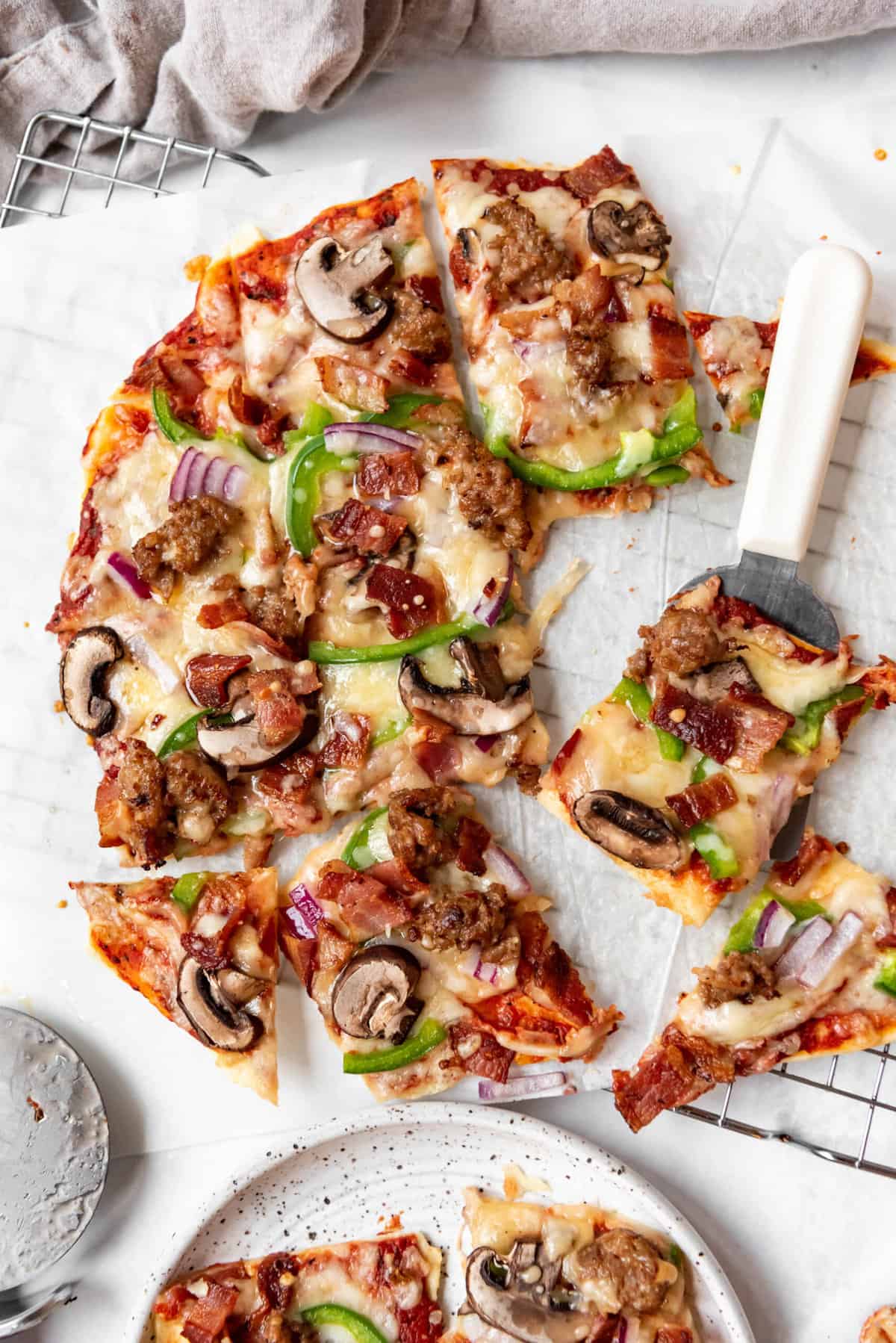 A deluxe St. Louis-style pizza cut into squares with one piece on a white handled spatula.