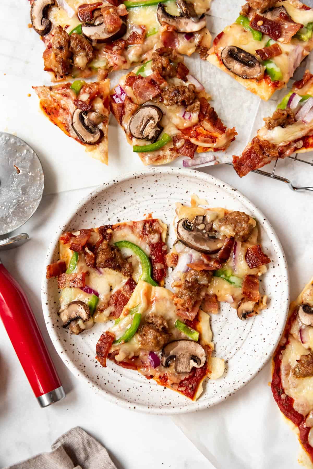 Slices of St. Louis-style pizza with meat and veggies on a plate next to a pizza cutter.