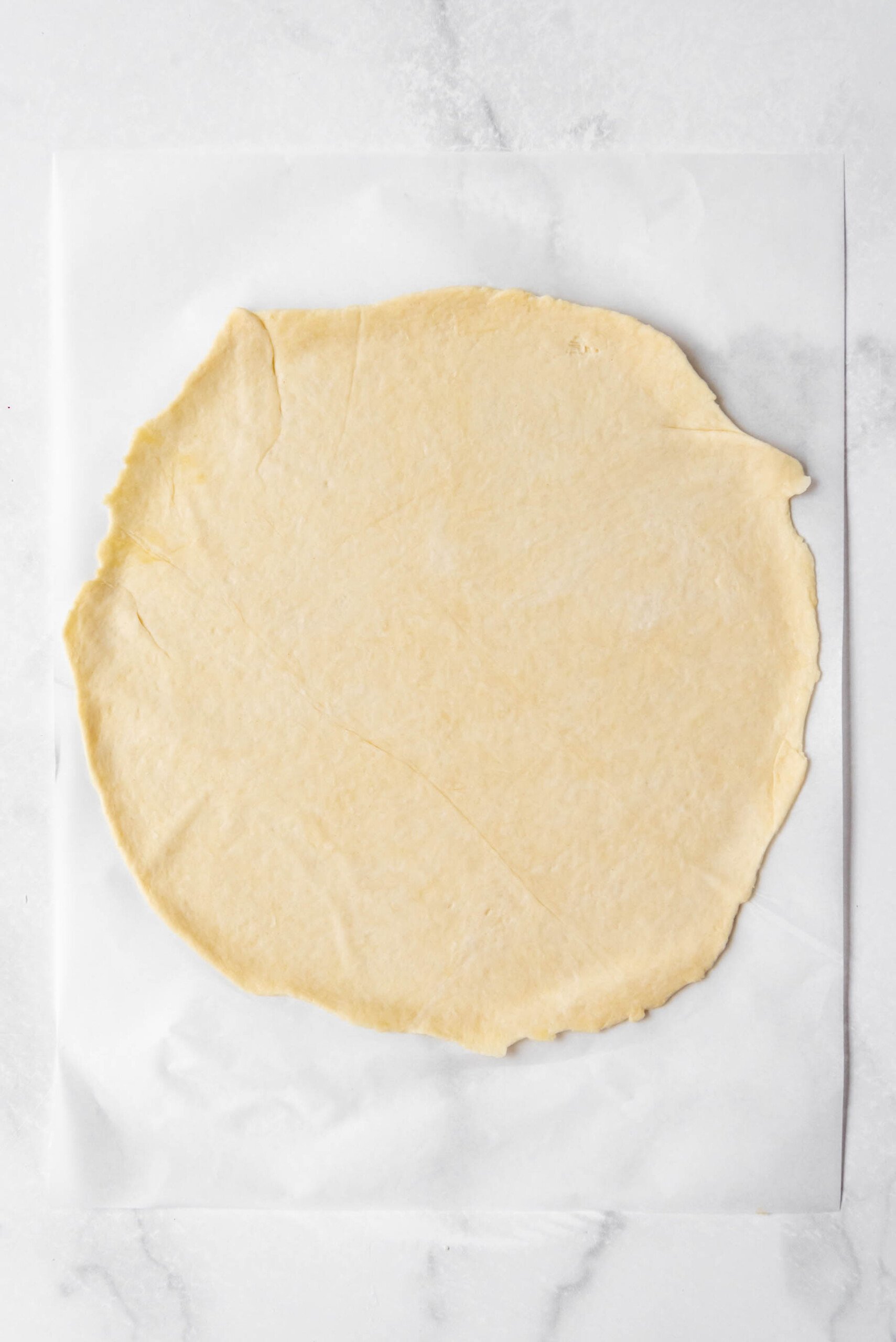 A pizza crust rolled out thin on parchment paper.
