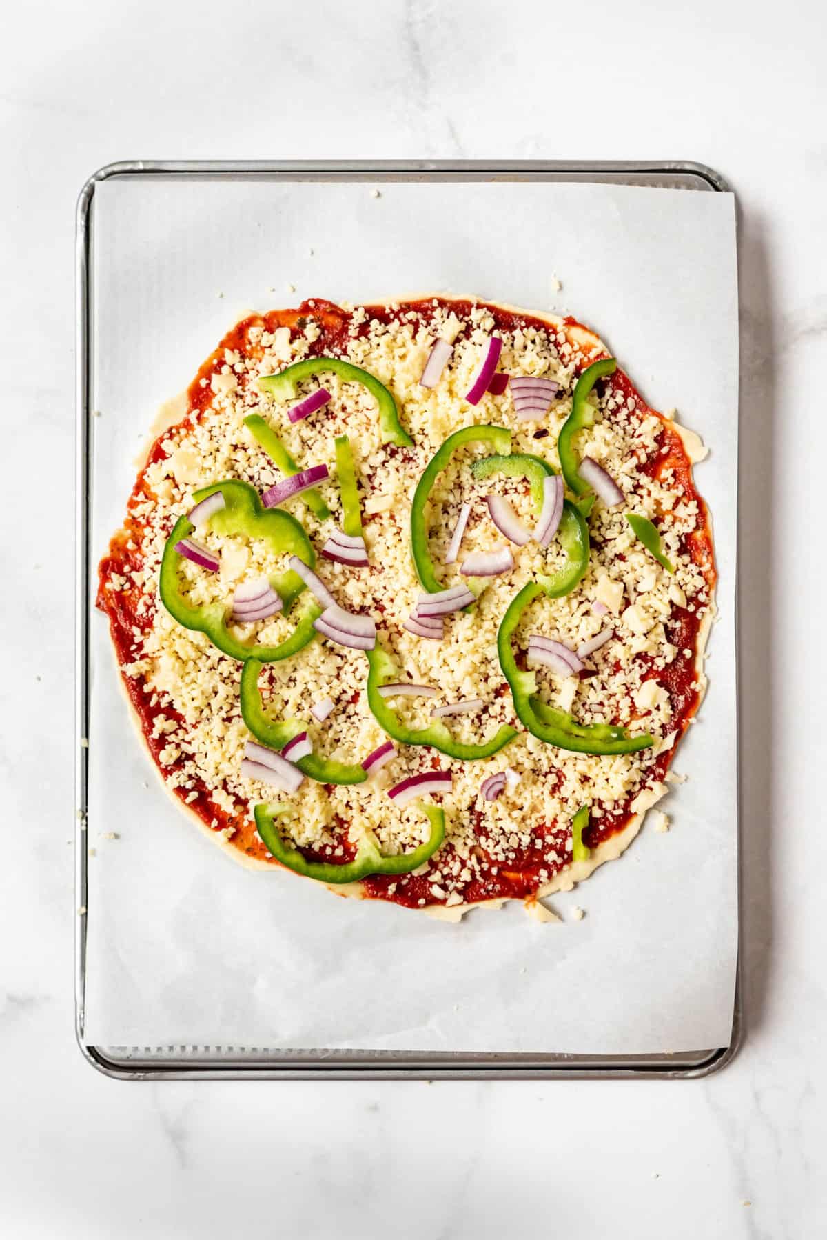 Sprinkled cheese, sliced green bell peppers, and sliced red onions on a pizza crust with sauce.