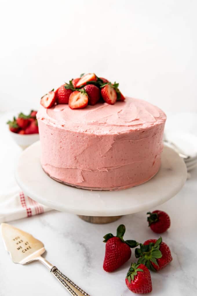 Close up of strawberry cake covered in pink frosting and topped with fresh strawberries.