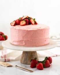 Impressive Strawberry Cake with strawberry frosting and strawberries on top on a cake stand.