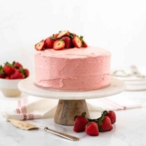 Impressive Strawberry Cake with strawberry frosting and strawberries on top on a cake stand.