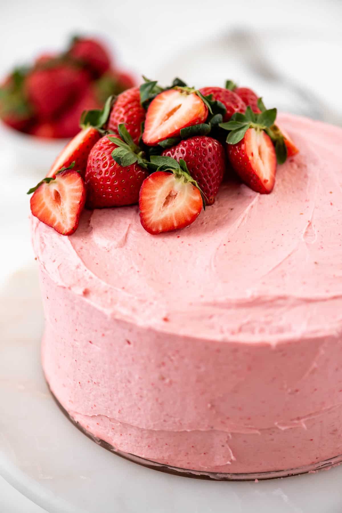 Close up of strawberry cake with strawberry frosting and fresh strawberries on top. 