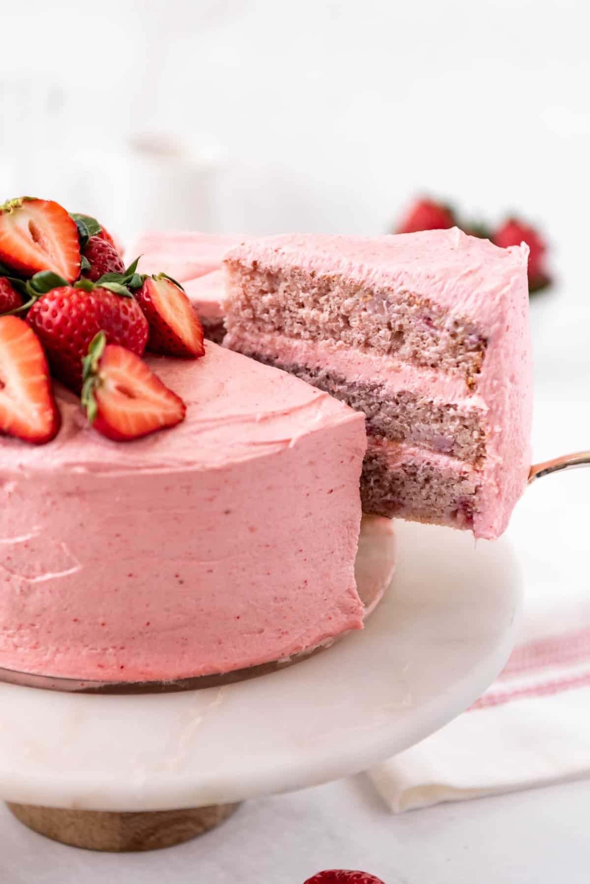 A slice of strawberry cake being lifted out of the full cake.