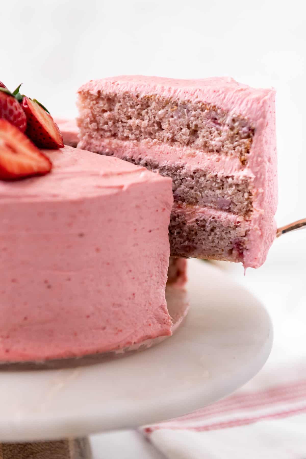 Close up of a slice of strawberry cake being lifted out of the full cake.