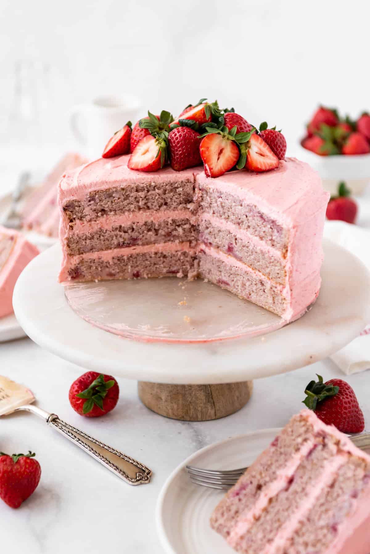 Hero shot of a strawberry cake eith slices cut out of it on a cake stand. 