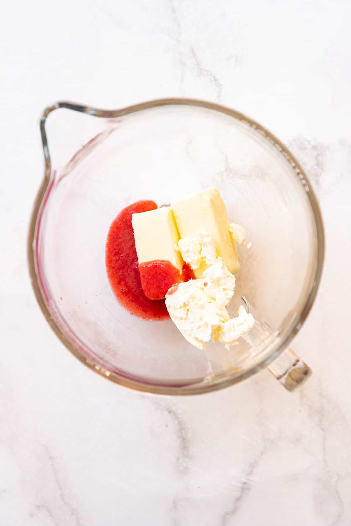 Top view of glass mixing jug with butter, crea cheese and strawberry puree in it. 