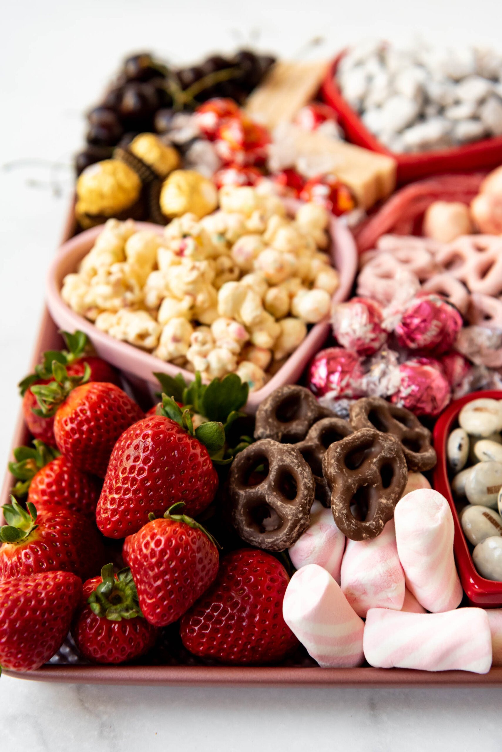 Strawberries, chocolate covered pretzels, marshmallows, and popcorn on a Valentine's Day dessert charcuterie board.